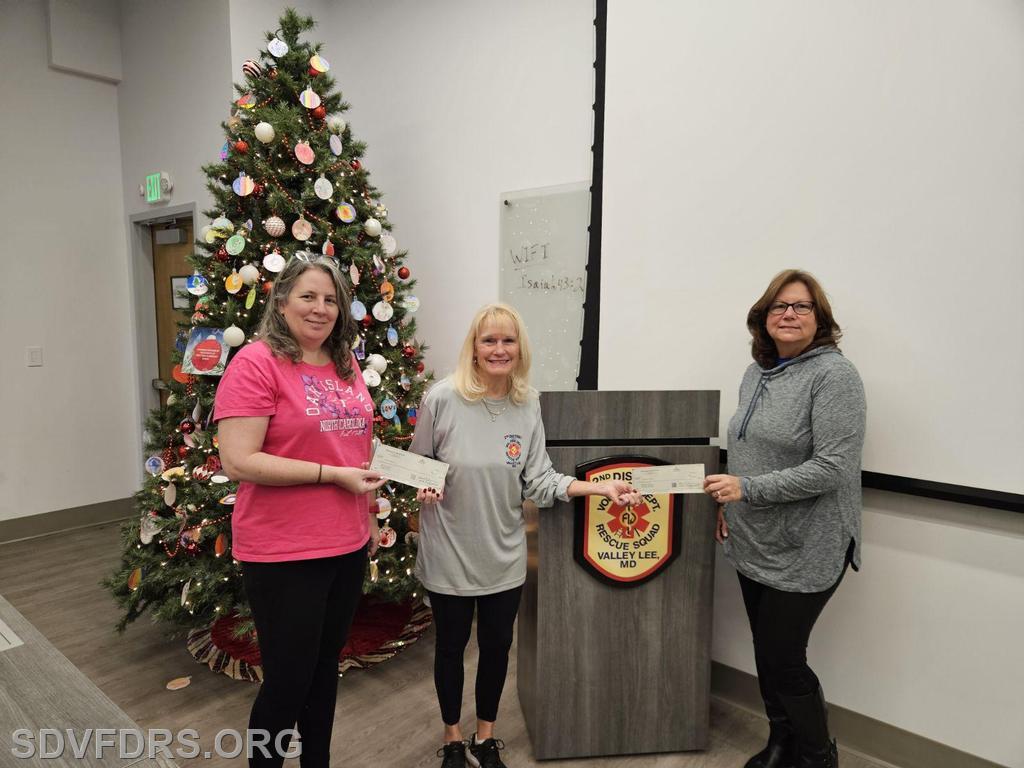 DeeDee Johnson, Fundraising Committee Chair, presents checks for $500.00, 3rd place prize to Wendy Van Noordt (left) of Drayden, and the 1st place prize of $10,000.00 to Cathy Caulder (right) of Tall Timbers.